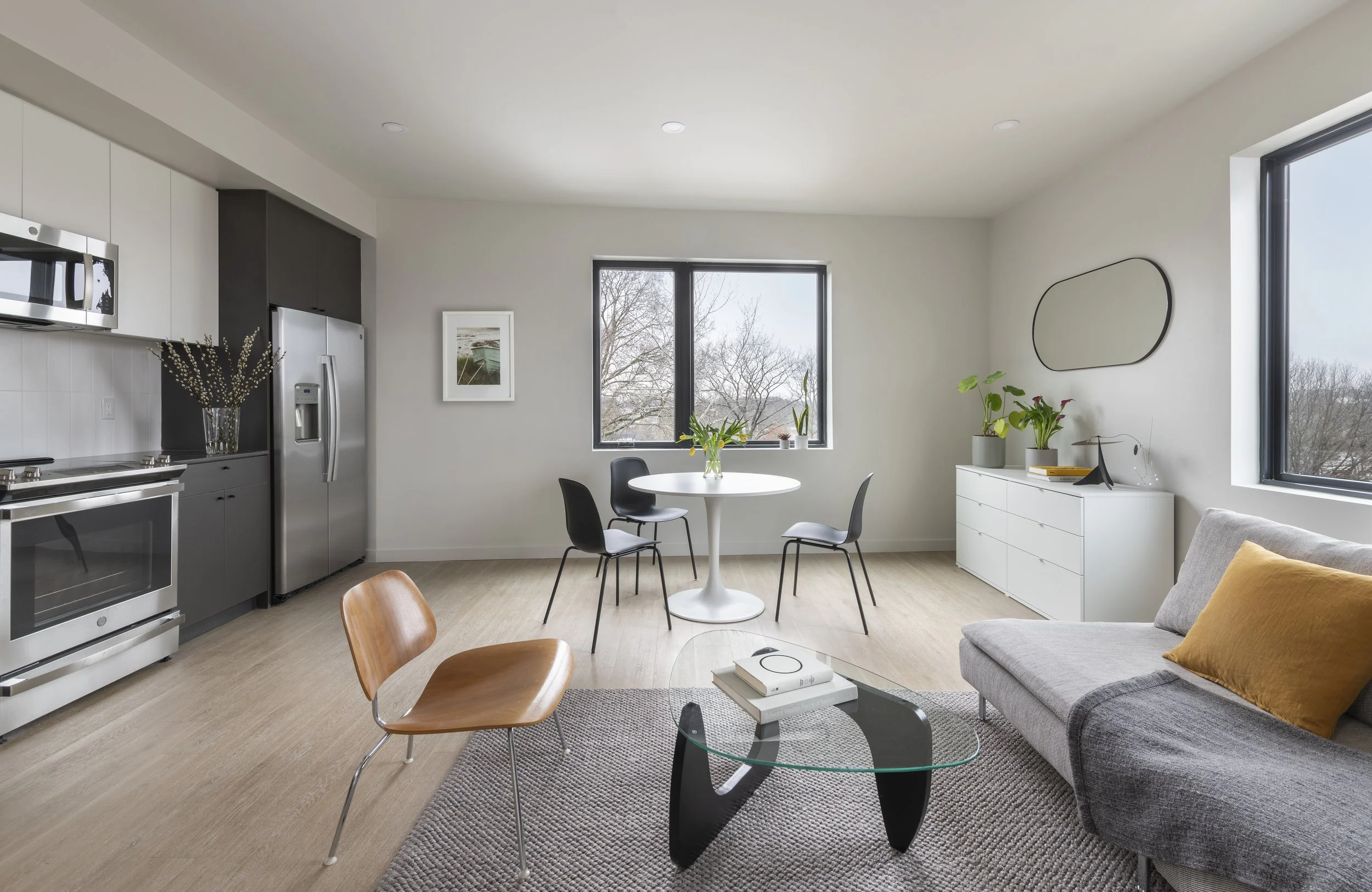 Open-concept apartment living room with kitchen, dining area, natural light and treetop views